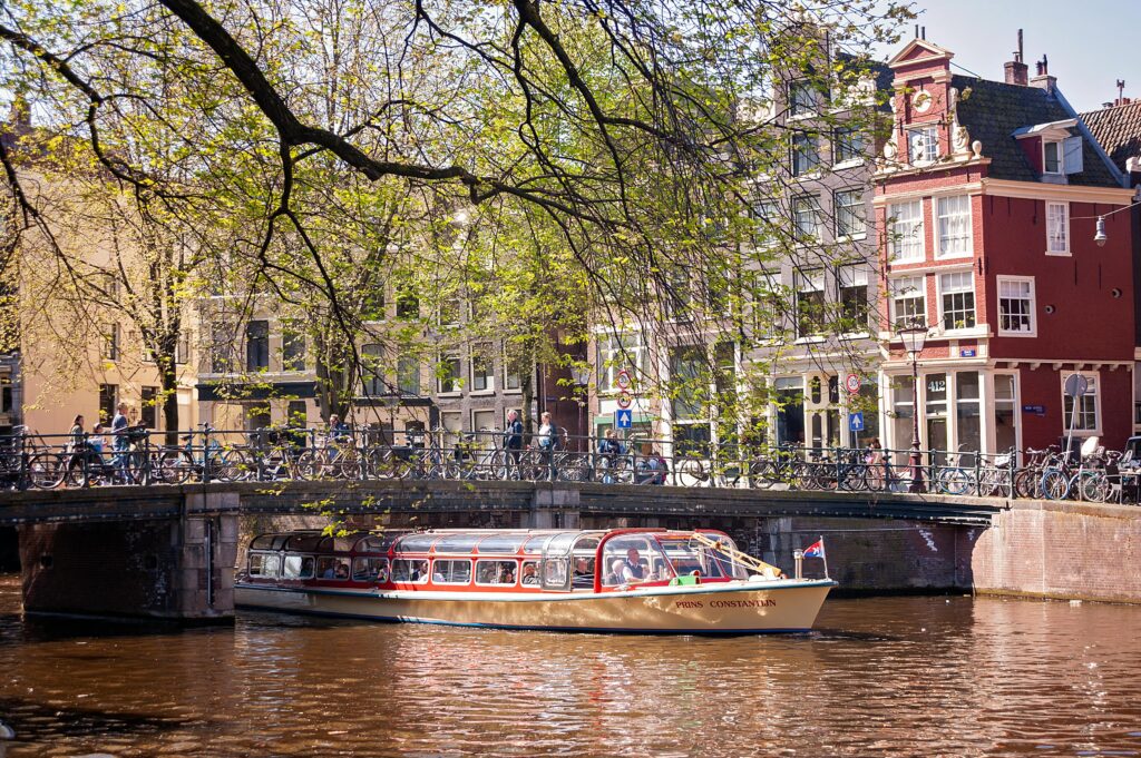 Picturesque Amsterdam canal view featuring a tour boat passing under a classic Dutch bridge.