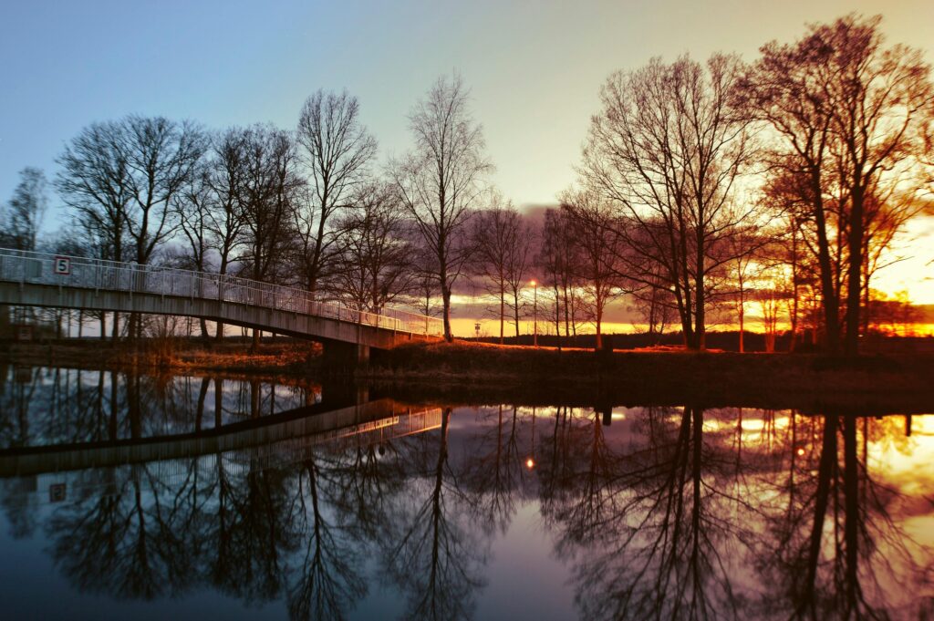 Beautiful sunset over a Swedish bridge with trees reflected on a calm lake.